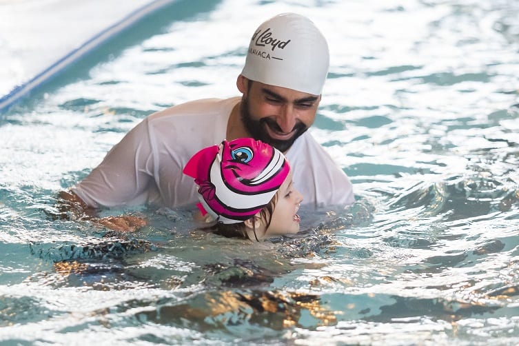A young boy in the swimming pool with the an instructor